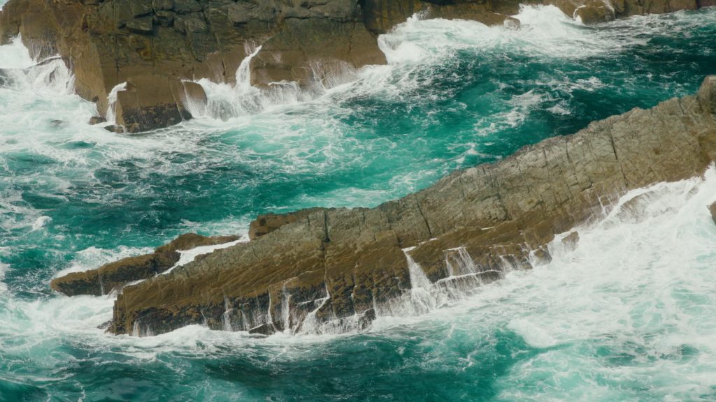 Close-up of water crashing over jagged rocks at the base of Kerry Cliffs, Ireland