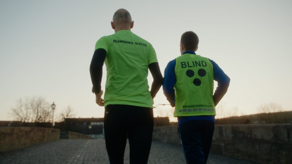 Tracking shot of blind runner Stefen Orben and his guide running at dusk