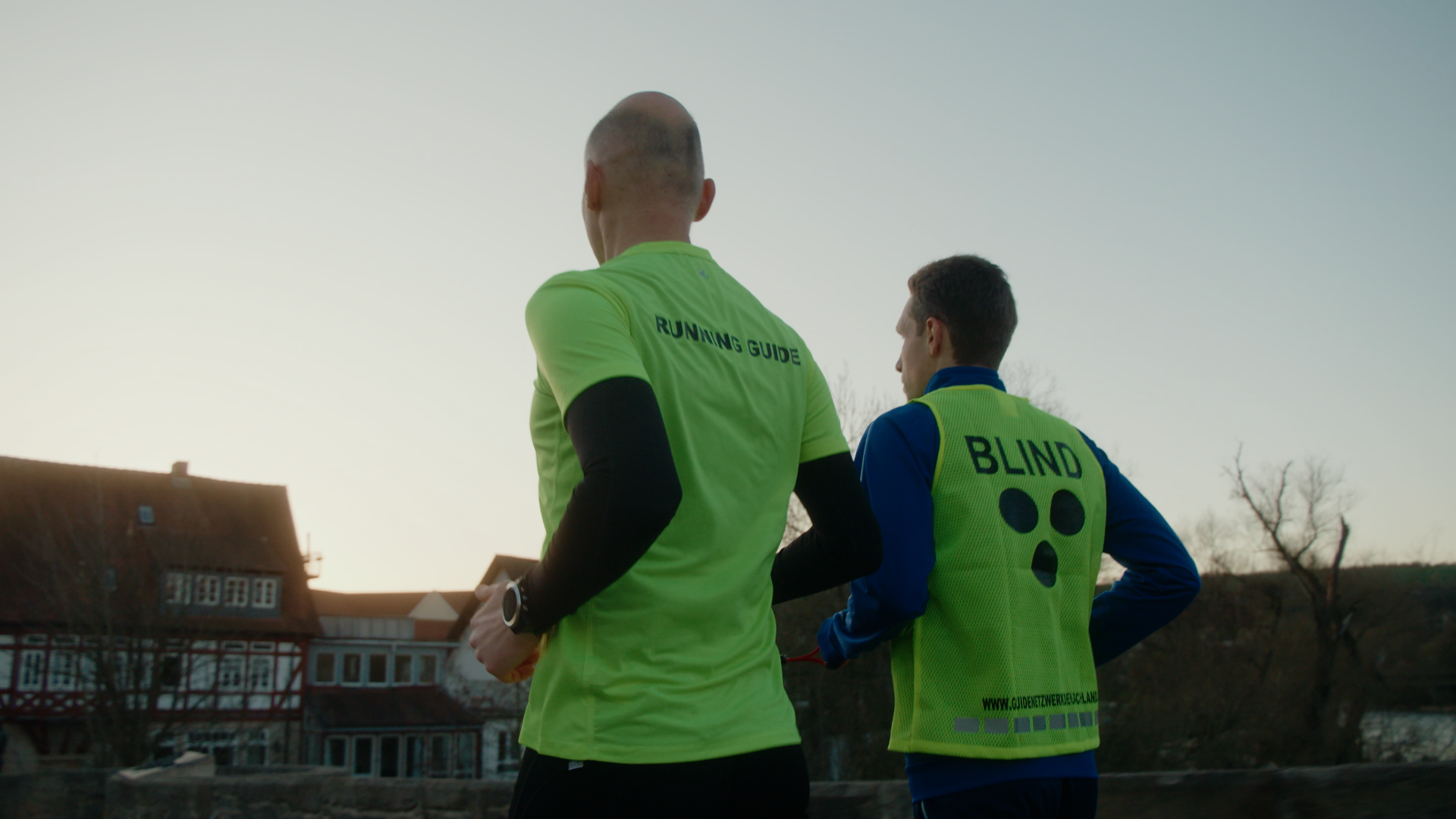 Handheld shot of Blind athlete running with his guide at dusk.
