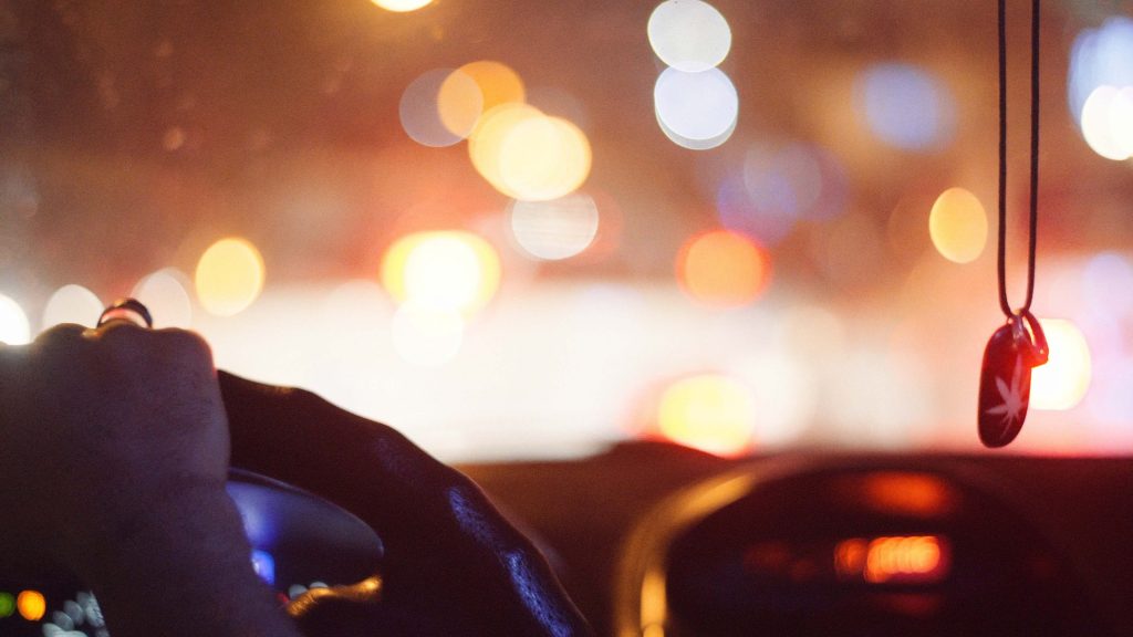 Telephoto shot of blurry taillights of cars seen behind the steering wheel of a car
