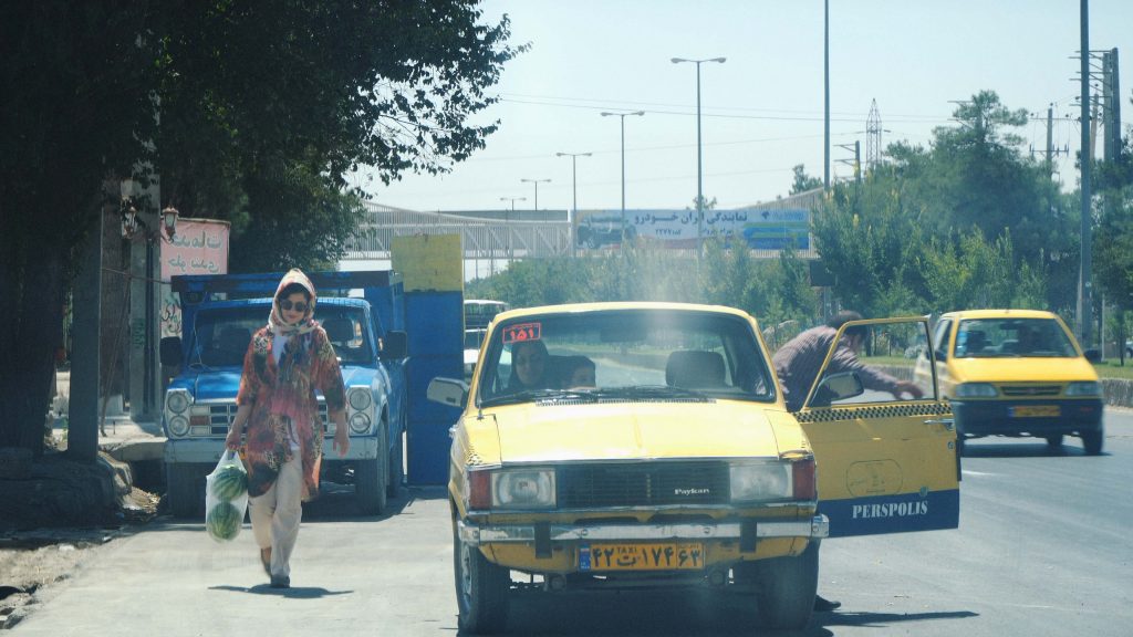 Telephoto of a woman purchasing watermelons at a market and carrying them back to her car
