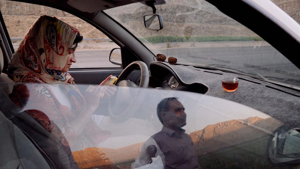 Man and woman taking a break from driving and drinking tea during sunset in Iran