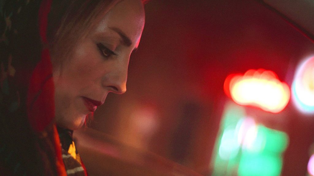 Woman in makeup and head scarf illuminated by neon streetlights in Yazd