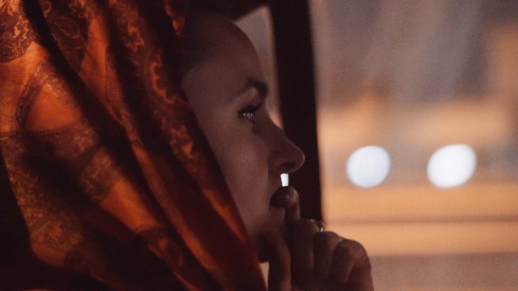 Contemplative portrait of Kristina Schlick in the car, illuminated by dashboard lights during night drive to the airport in Tehran