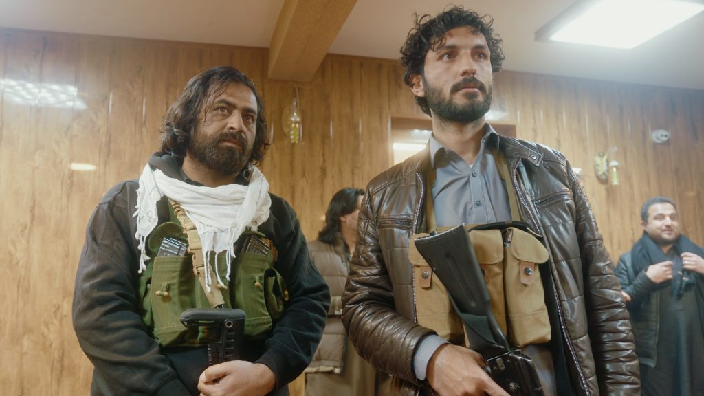 Two bodyguards watching cricket on TV inside a restaurant