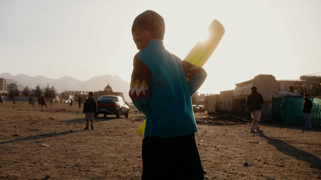 Silhouetted boy playing cricket in backlight during golden hour