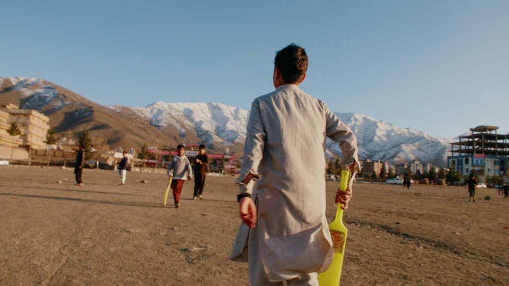 Tracking shot of young street cricket player in front of Kabul mountain range