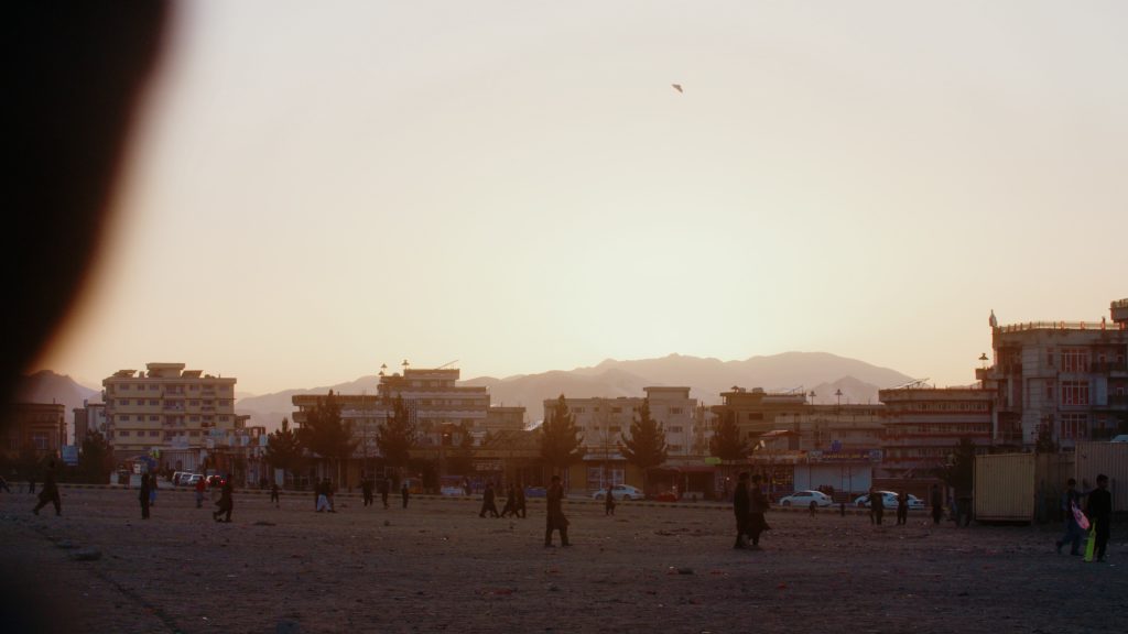 Golden-hour light behind street cricket field with Kabul’s mountain range in the background