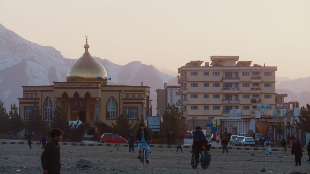 Children riding bicycles in Kabul in front of a mosque at sunset