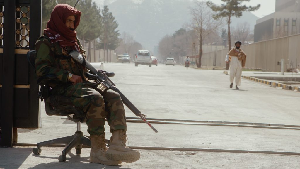 Taliban fighter seated casually on office chair with M16 at checkpoint entering Kabul’s former Green Zone