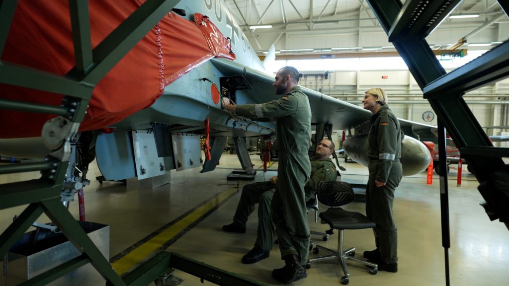 Wide-angle view of mechanics examining Eurofighter's computer system during routine maintenance check